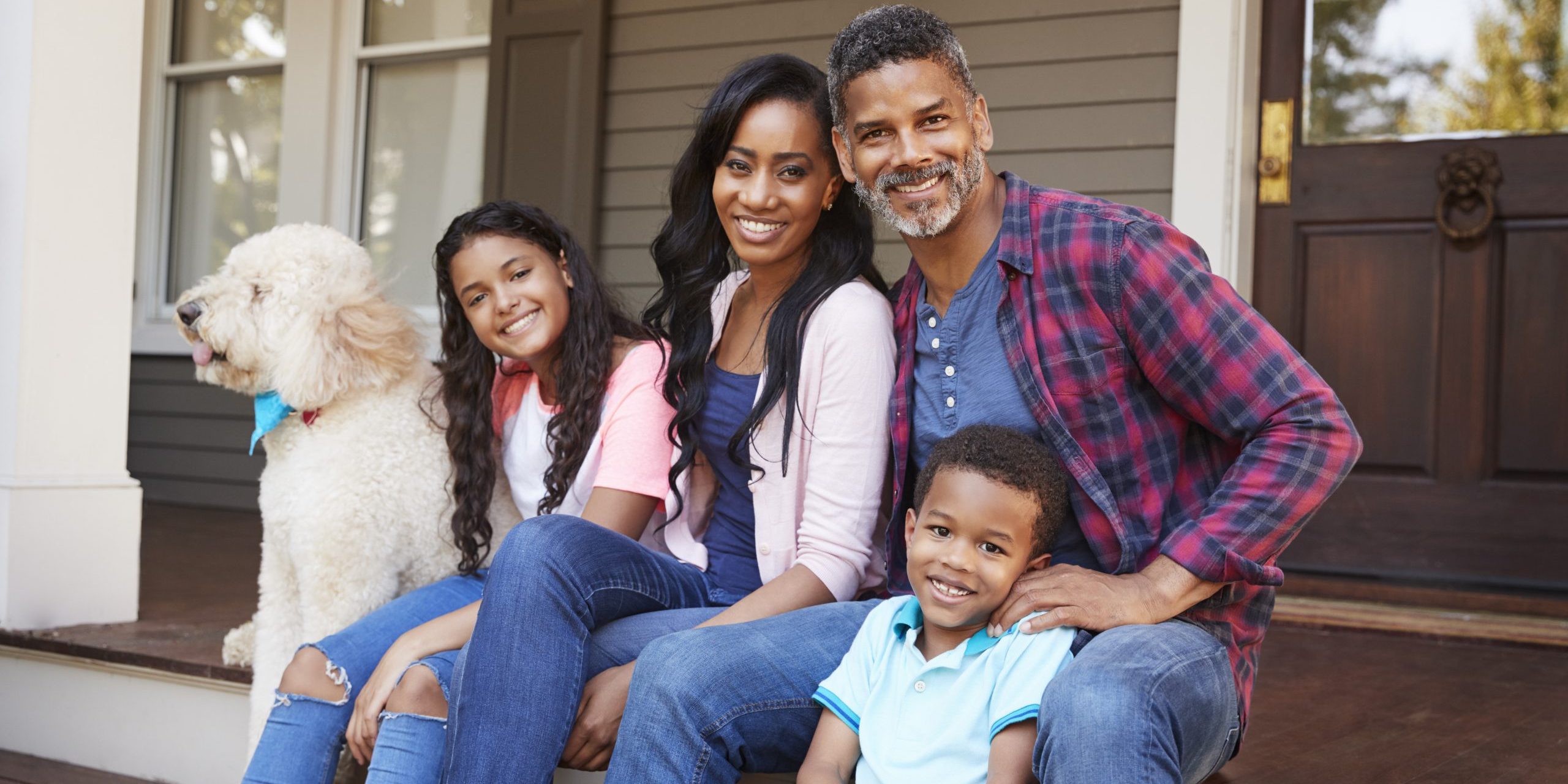 Family With Children And Pet Dog Sit On Steps Of Home